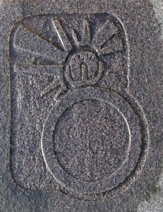 Detail of ring with rays of light emitting from it carved in shallow relief on a (possibly granite) stone block.