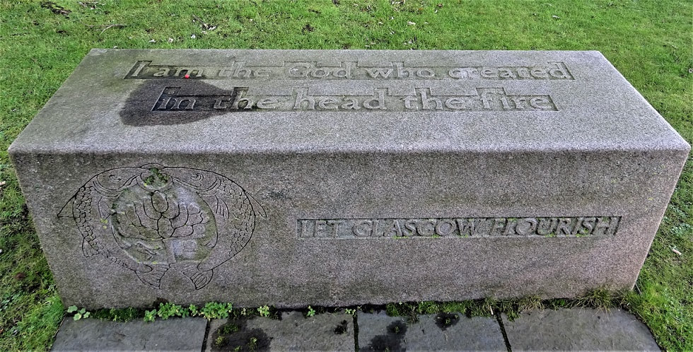 (possibly granite) rectangular stone block with CoA and text carved in shallow relief. Front facing surface has CoA and text: "Let Glasgow Flourish". Top surface text: "I am the god who created / in the head the fire" (https://allpoetry.com/poem/8611863-The-Mystery-by-Amergin-Glangel)